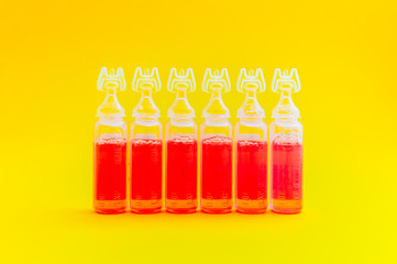 Abstract medical background, an ampoules with red liquid. A group of vaccine in bottles on a yellow background.