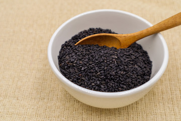 Black sesame seeds in white cups and wooden spoons on brown tablecloths are suitable for graphic or vocal work.