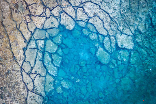 An aerial view of the beautiful Mediterranean Sea, where you can see the cracked rocky textured underwater corals and the clean turquoise water of Protaras, Cyprus