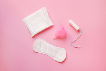 women intimate hygiene products - sanitary pads, menstrual cup and tampon isolated on pastel pink background, top view, flat lay