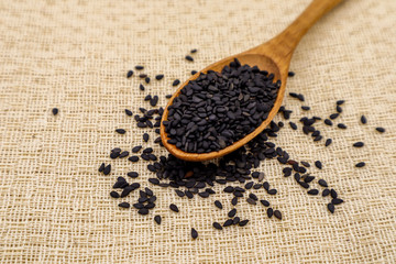 Black sesame seeds in white cups and wooden spoons on brown tablecloths are suitable for graphic or vocal work.