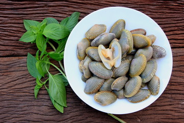 Stir fried clam with chili paste and thai basil leaf in white dish on brown wooden ,for Food preparation.