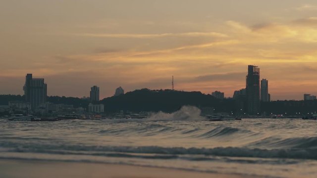 evening ocean with waves and silhouette of man riding water scooter against hotels and sunset sky