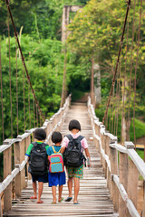 Asian primary school girls walking across a suspension footbridge at dusk.