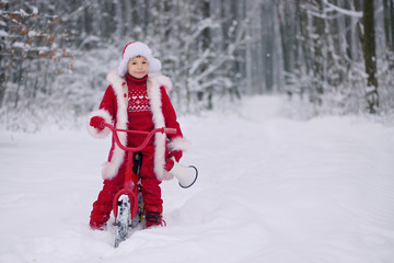Child dressed  as Santa Claus with gifts in snowy winter outdoors.