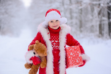 Child dressed  as Santa Claus with gifts in snowy winter outdoors.