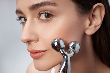 Attractive young woman with perfect skin using platinum facial massager