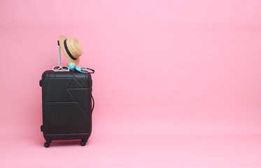 Black suitcase with sun glasses, hat  on pastel pink  background. travel concept. minimal style