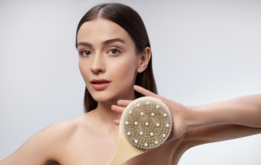 Charming young woman with massage brush standing against light blue background