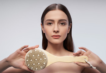 Pretty girl with massage brush standing against light blue background