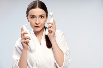 Beautiful young woman holding bottle of cosmetic cream and pore cleansing brush