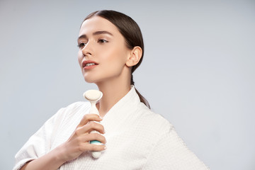 Attractive young woman in white bathrobe holding pore cleansing brush