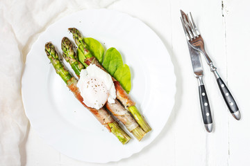 Grilled green asparagus wrapped with bacon, benedict poached egg on white wood background. Breakfast