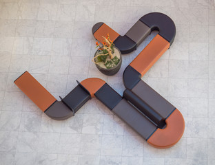 Top view of curved black and orange leather couch seating and flower pot in modern office hall with marble pavement