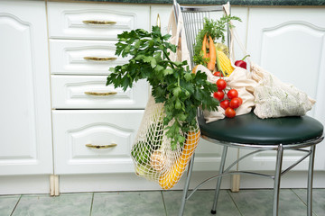 Fresh vegetables and greens in mesh bags for eco products lie on a chair. Zero waste concept.