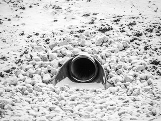 Closeup black and white view of a large storm water drainage culvert pipe emptying into a retention...