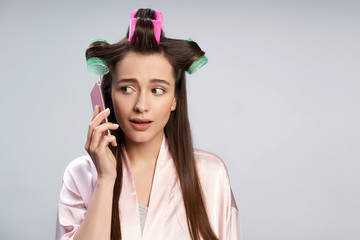 Beautiful young woman with curlers in hair talking on cellphone