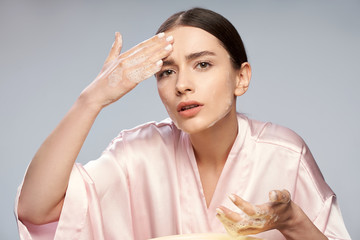 Charming young woman washing face with foaming cleanser