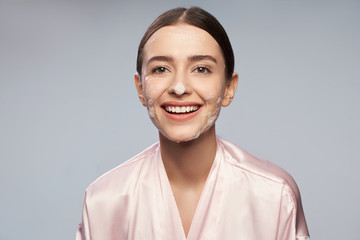 Fototapeta premium Pretty girl with purifying foam on face standing against light blue background