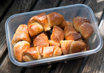 Homemade croissants with cherries in a plastic container isolated on wooden background.