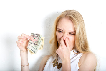 blonde squeezes her nose with her fingers from the smell of dollar bills. The concept of dirty money.