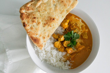 Bowl of Indian Butter Chicken with Jasmine Rice, Homemade Naan, and Cilantro, White Background, Closeup