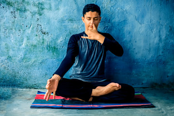 Portrait shot of the young man doing pranayama or pranayam or breath control yoga on a colorful mat with wearing black attire. - obrazy, fototapety, plakaty