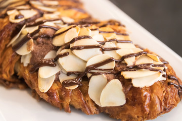 Croissant chocolate and almond sliced with chocolate sauce on white plate.