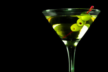 A martini glass with green olives on a black background