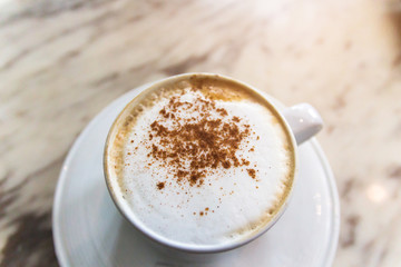 Cup of coffee with soft microfoam and cinnamon ground on marble table