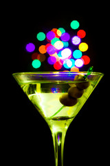 A martini glass with green olives on a black background