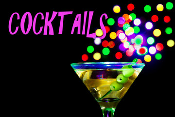 A martini glass with green olives on a black background