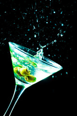A martini glass with green olives on a black background