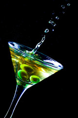 A martini glass with green olives on a black background