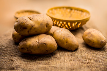 Close up shot of potato or aloo or alu on jute bag surface along with two vegetable and fruit...