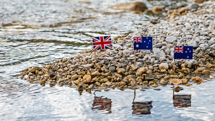 commonwealth flags reflected in the water of the rocky riverbank