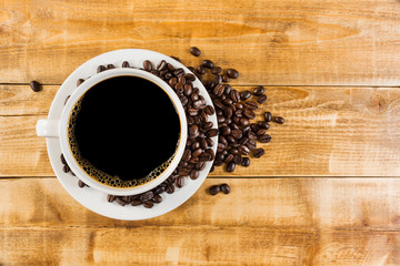 Black coffee in a white coffee cup And roasted coffee beans placed on the old wooden floor, top view
