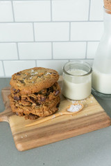 Stack of Homemade Salted Chocolate Chip Cookies with glass of milk, White Subway Tile Background, Wooden Plate