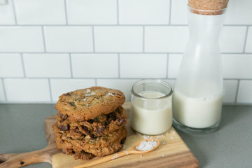 Stack of Homemade Salted Chocolate Chip Cookies with glass of milk, White Subway Tile Background, Wooden Plate