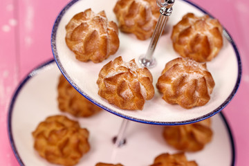Freshly baked eclairs with icing sugar on a beautiful platform on a pink background.