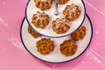 Freshly baked eclairs with icing sugar on a beautiful platform on a pink background.
