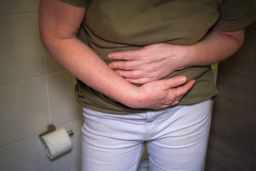 woman stands in the toilet and holds on to a sore stomach.