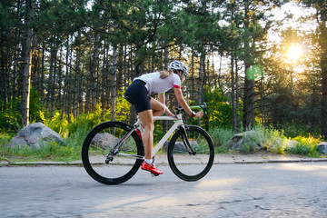 Young Woman Cyclist Riding Road Bicycle on the Free Road in the Forest at Hot Summer Day. Healthy Lifestyle Concept.