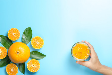 Hand of woman holding glass of orange juice and orange fruits with sliced pieces and leaves on blue background, flat design