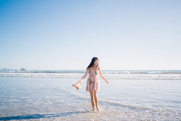 Fototapeta premium Young Asian woman walking on beach. Beautiful female happy relax walking on beach near sea when sunset in evening. Lifestyle women travel on beach concept.