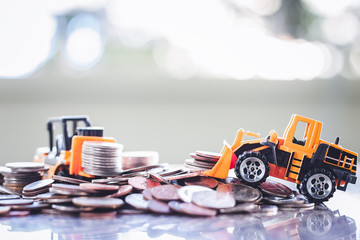The yellow toy heavy machinery includes bulldozer and forklift with pile of coins against blurred background for saving money, investment, business and finance concept © Kesinee