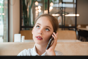 Portrait of child behind a laptop in cafe. Internet and telephone communications.