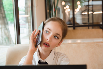 Portrait of child behind a laptop in cafe. Internet and telephone communications.