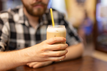 Hands of a stylish young man in a plaid shirt holding cocoa in his hands into a glass with a straw in one hand and a smartphone in the other hand. Cafe recreation with high speed internet concept.