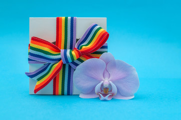 white gift box with rainbow ribbon and Orchid flower on blue background copy space